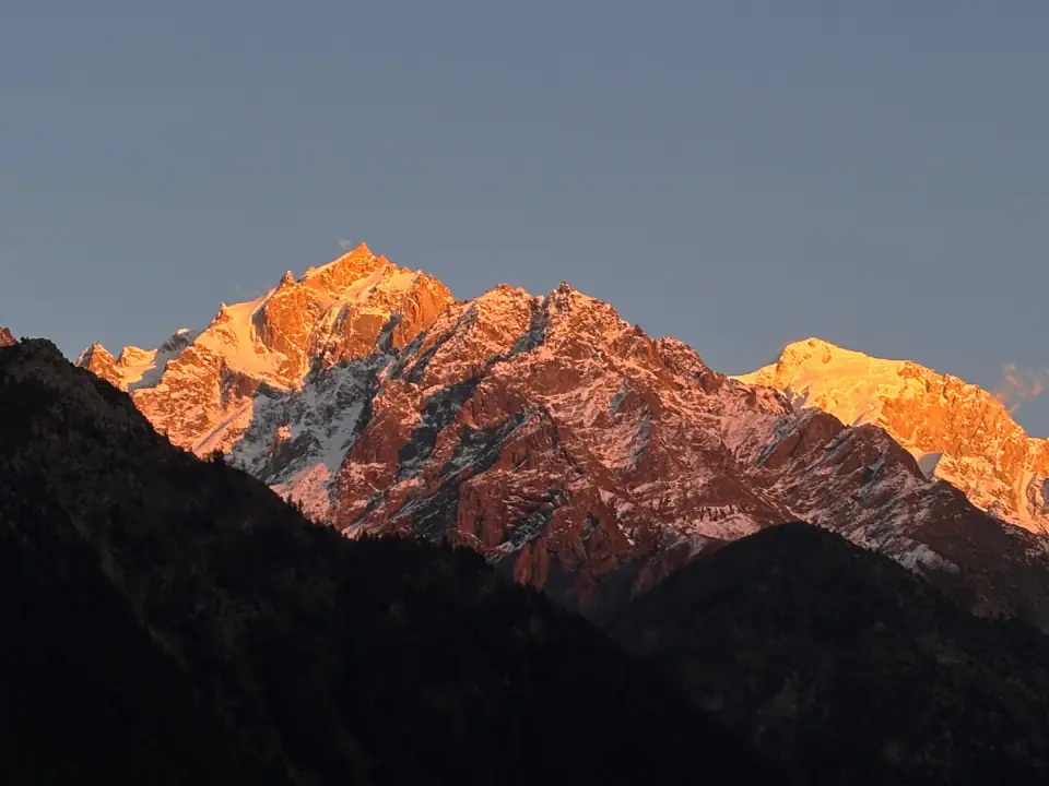 Snow-covered mountain peaks and ridges glowing with golden light under a clear morning sky.