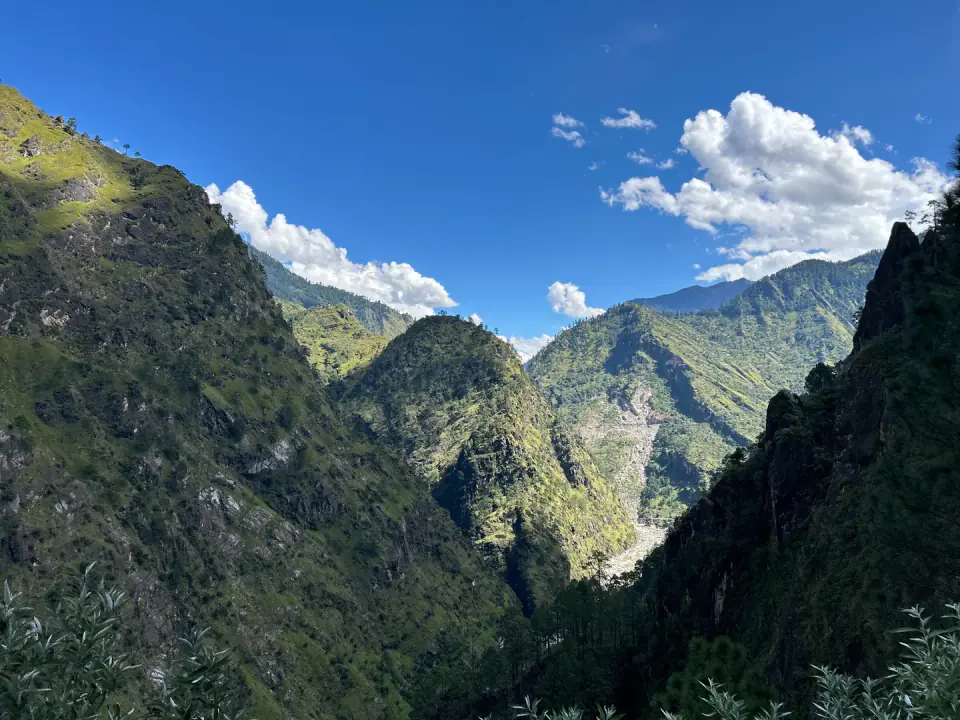 A wide rocky riverbed winding through a steep green mountain gorge under bright daylight.
