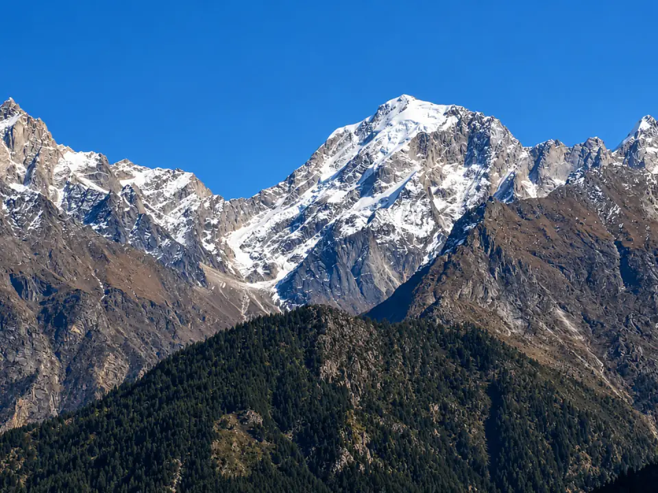 Dramatic snow-dusted mountain ridges and sheer cliffs towering under a vibrant clear blue sky.